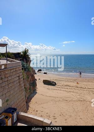 Incantevole spiaggia a Cascais in Portogallo con onde calme scalinata di pietra dorata e tradizionali case sul mare che costeggiano la costa in una giornata di sole Foto Stock