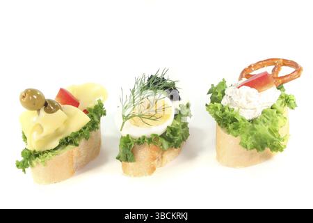 Canape con insalata, formaggio, formaggio spalmabile e uova su sfondo bianco Foto Stock
