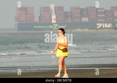 Isola di Palms, Stati Uniti. 20 maggio 2025. Una giovane donna cammina lungo la spiaggia mentre la nave portacontainer Zim Mount Everest tira attraverso il canale nel porto di Charleston, il 20 maggio 2025 a Isle of Palms, South Carolina. A causa delle tariffe globali imposte dal presidente degli Stati Uniti Donald Trump, il traffico merci verso Charleston è pianeggiante dopo due mesi di crescita consecutiva. Crediti: Richard Ellis/Richard Ellis/Alamy Live News Foto Stock