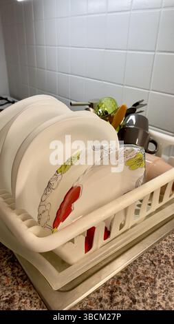Piatti puliti organizzati in una griglia di asciugatura in una cucina moderna con piastrelle bianche e arredamento minimalista Foto Stock