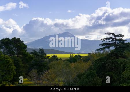 Paesaggio mozzafiato caratterizzato da una montagna prominente che si innalza sopra una vibrante valle, con un cielo nuvoloso che crea uno sfondo drammatico Foto Stock