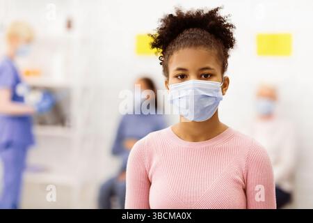 African Girl in posa indossando Coronavirus maschera viso in piedi in ospedale Foto Stock