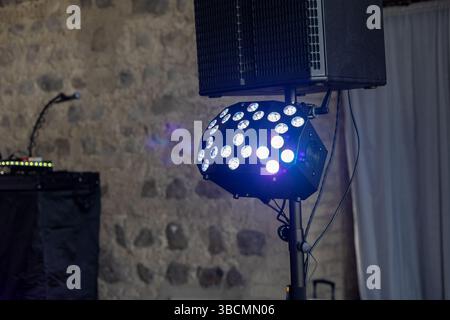 Le luminose luci LED sono posizionate su un piedistallo, pronte ad illuminare un'esibizione musicale in un locale rustico caratterizzato da pareti in pietra a vista e un vivace atmo Foto Stock