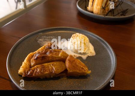 Focalizzazione selettiva sulla torta di mele con cannella cosparsa servita con palla di gelato in un piatto. Con metà di mele su pasta sfoglia. Foto Stock