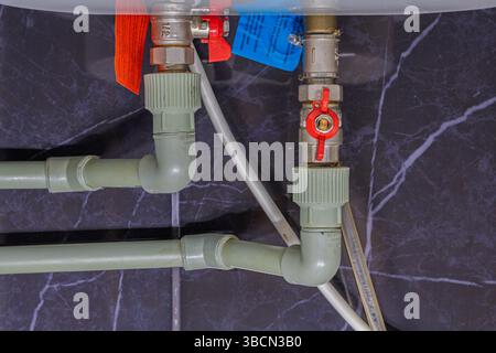 Due valvole su tubi in plastica e connettori in metallo sulla caldaia con acqua calda in uscita e fredda in entrata. Interruttori rossi aperti. L'acqua calda e fredda è erba cipollina Foto Stock