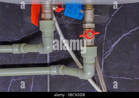 Due valvole su tubi in plastica e connettori in metallo sulla caldaia con acqua calda in uscita e fredda in entrata. Interruttori rossi chiusi. L'acqua calda e fredda è erba cipollina Foto Stock