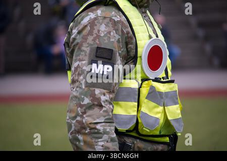 Immagine ravvicinata di un ufficiale di polizia militare che indossa un'uniforme mimetica e un vivace giubbotto di sicurezza in piedi all'aperto durante il giorno. L'agente porta una t Foto Stock