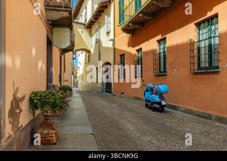 Uno scooter blu parcheggiato contro il muro arancione sul vicolo acciottolato nel centro storico di Alba, Italia. Foto Stock