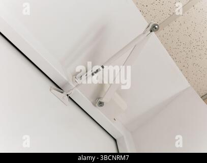 Vista dal basso verso l'alto di un chiudiporta installato su uno sportello bianco in metallo. Foto Stock