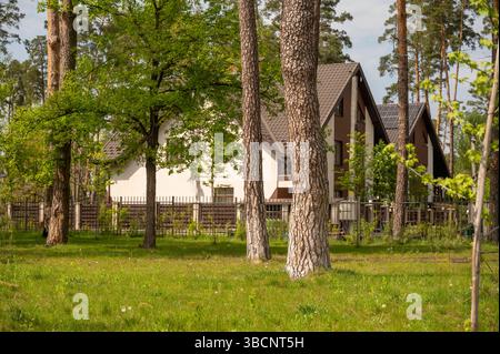 Case residenziali bianche nel villaggio circondate da pineta nei raggi luminosi del sole che tramonta Foto Stock