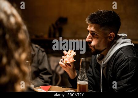 Gli amici si godono la pizza e le bevande in un accogliente ristorante durante una riunione serale Foto Stock