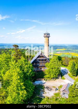 La vista aerea cattura la torre di osservazione di Svatobor circondata da alberi lussureggianti e colline della Cechia. La giornata di sole rivela colori vivaci del paesaggio, invitanti esplorazioni e divertimento. Foto Stock