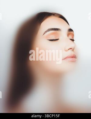 Ritratto contemporaneo. Bella donna con trucco impeccabile e occhi chiusi, tranquilla con luce soffusa e sfondo sfocato. Foto Stock