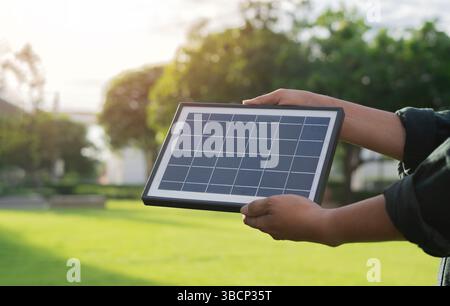 Vista laterale dell'uomo che tiene in mano il pannello solare portatile con luce solare riflessa nel parco cittadino. Energia alternativa, energia rinnovabile. Foto Stock