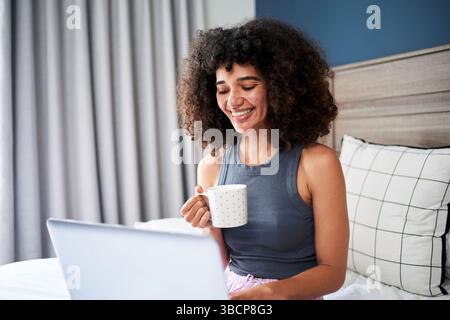 Una giovane donna che lavora da casa sorride e beve un caffè in un ambiente rilassato al mattino Foto Stock