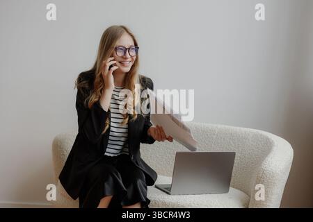 Donna professionista al telefono mentre esamina documenti in un moderno ambiente di lavoro durante il giorno Foto Stock