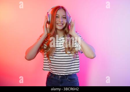Una giovane donna ama la musica con le cuffie mentre sorride in uno sfondo colorato durante un momento di divertimento a casa Foto Stock