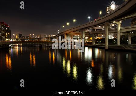 Viadotto sopraelevato illuminato di notte, che si riflette nelle acque del fiume Tokyo sotto un cielo buio Foto Stock