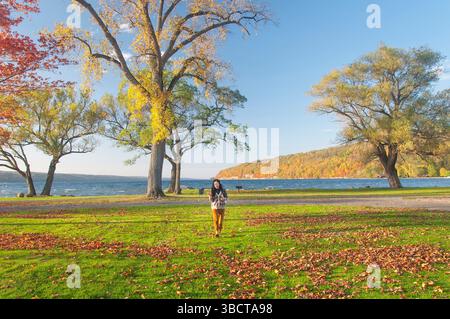 Una donna cinese che cammina attraverso Clute Park sul lago Seneca nel tardo pomeriggio al tramonto in autunno nella parte settentrionale dello stato di New york. Foto Stock