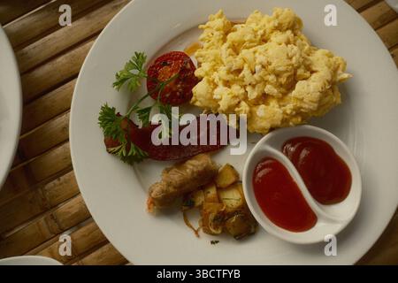 Un piatto da colazione con uova strapazzate, pomodoro alla griglia, pancetta croccante, salsiccia, patate saltate, e ketchup Foto Stock