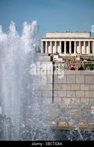 WASHINGTON DC - la fontana del World War II Memorial si erge in modo prominente sul National Mall, con l'iconico Lincoln Memorial visibile in lontananza. Completato nel 2004, il World War II Memorial onora i 16 milioni di americani che hanno prestato servizio nelle forze armate durante la guerra, tra cui più di 400.000 che hanno perso la vita. Il monumento presenta una piscina arcobaleno centrale circondata da 56 pilastri di granito che rappresentano gli stati e i territori degli Stati Uniti durante la guerra. Situato all'estremità orientale della piscina riflettente, il monumento crea un collegamento visivo tra il Lincoln Memorial e il Washington Monument Foto Stock