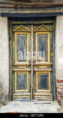 Primo piano di una porta in legno vintage con vernice resistente agli agenti atmosferici e ricche texture in una vecchia strada europea. Cattura la storia, il decadimento e il carattere dell'ar urbano Foto Stock