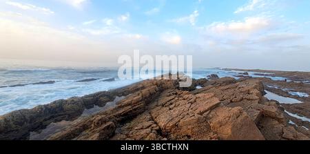 Vista panoramica delle onde dell'oceano che si infrangono contro una costa rocciosa durante una splendida alba Foto Stock
