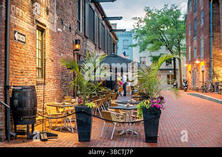 Virtue Feed and Grain Restaurant posti a sedere all'aperto Alexandria Virginia // ALEXANDRIA, Virginia - posti a sedere all'aperto al Virtue Feed and Grain Restaurant nel quartiere storico di Old Town Alexandria. Il ristorante, ospitato in un magazzino ristrutturato del XIX secolo che un tempo serviva come negozio di alimenti e cereali, offre ai clienti opzioni per mangiare all'aperto. Situato a solo un isolato dal lungomare del fiume Potomac al 106 di South Union Street, lo spazio all'aperto consente ai commensali di gustare i pasti mentre si sperimenta il fascino storico della città vecchia di Alexandria. Foto Stock