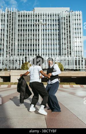 Due donne africane che ballano e si divertono all'aperto in una piazza urbana Foto Stock