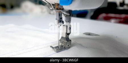 Primo piano dell'ago della macchina da cucire cucendo rapidamente il tessuto bianco in una fabbrica tessile, dimostrando la precisione e la velocità di cucito industriale Foto Stock