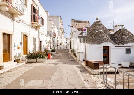 Una tranquilla e stretta strada ad Alberobello, in Italia, fiancheggiata da tradizionali case a trulli con tetti conici in pietra, pareti bianche e vegetazione in vaso. Un fascino intramontabile del sud Foto Stock