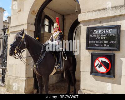 Il Household Cavalry Life Guards accanto al segnale di avvertimento che il cavallo può mordere, Whitehall, Londra, Regno Unito Foto Stock