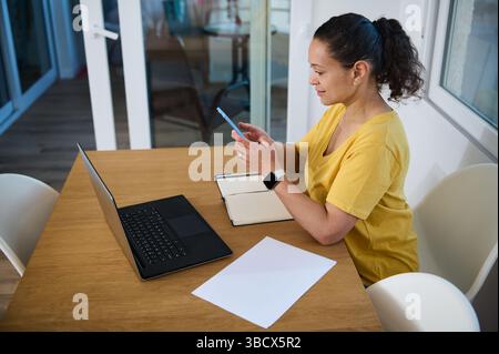 Donna professionale che lavora in remoto in un accogliente ufficio domestico minimalista, che naviga nella tecnologia e che bilancia le attività in modo efficiente, incarna i moderni freelance Foto Stock