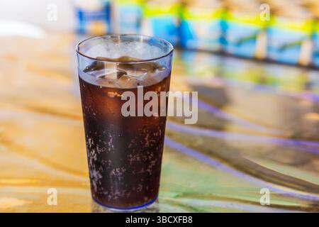 Bicchiere di cola con ghiaccio e condensa visibile sulla superficie in piedi su un colorato tavolo riflettente con sfocatura dello sfondo. Aruba. Foto Stock