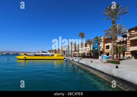 Vivace porticciolo del Mar Rosso con edifici colorati, palme e una barca gialla luminosa sotto il cielo azzurro in una popolare località turistica egiziana. Foto Stock