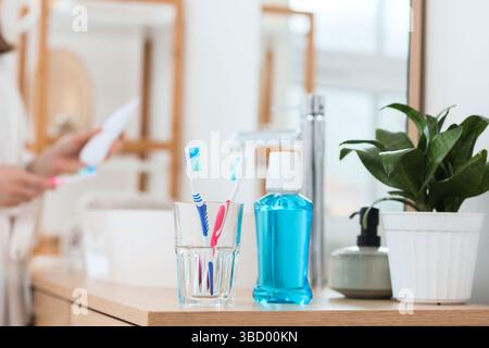 Vetro con spazzolini da denti e risciacquo per la bocca sul tavolo in bagno Foto Stock