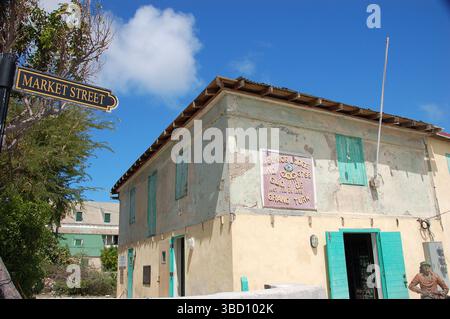 Vecchio edificio in stile caraibico con persiane turchesi su Front Street, Grand Turk, con un uomo seduto all'esterno sotto il luminoso sole tropicale Foto Stock