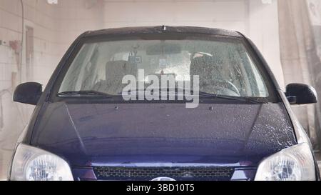 L'auto passa attraverso l'autolavaggio automatico e viene bagnata e risciacquata Foto Stock