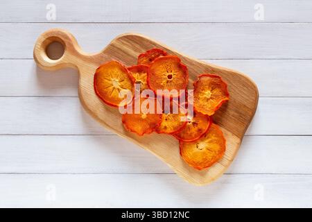 Fette di cachi essiccate visualizzate su un piccolo tagliere di legno su uno sfondo bianco del tavolo di legno Foto Stock