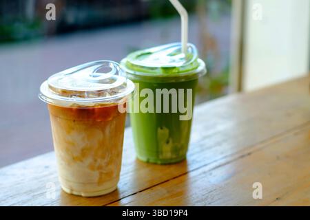 Primo piano di tè verde matcha ghiacciato e latte cremoso in tazze di plastica su un tavolo di legno, che mette in mostra lo stile di vita moderno del caffè, l'illuminazione naturale e il rinfresco Foto Stock