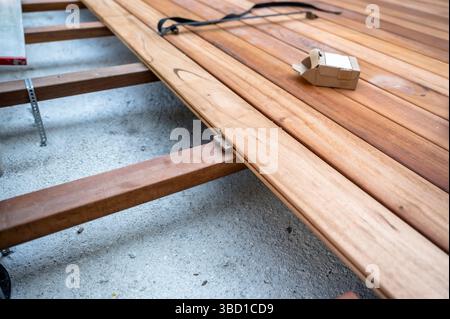 Vista ravvicinata delle tavole del ponte in legno installate utilizzando dispositivi di fissaggio nascosti su un sottotelaio. L'immagine mostra una fase di costruzione con attrezzi e materiale Foto Stock