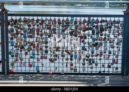 Numerosi lucchetti d'amore colorati sono appesi su un ponte che sovrasta un fiume panoramico, a simboleggiare l'affetto e l'impegno duraturi. L'acqua serena nel Foto Stock