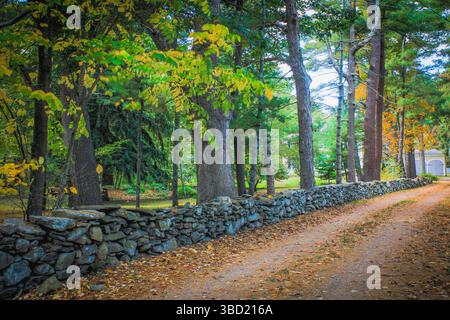 La magia autunnale del New England: Una strada sterrata si snoda oltre una parete di mattoni intemprati, che si illumina di colori autunnali. Pura bellezza rustica! Foto Stock