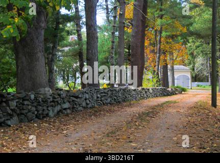 La magia autunnale del New England: Una strada sterrata si snoda oltre una parete di mattoni intemprati, che si illumina di colori autunnali. Pura bellezza rustica! Foto Stock