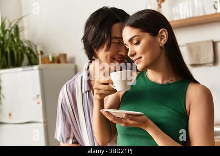 Una coppia gioiosa si gode un momento tenero a casa, condividendo caffè e sorridendo con calore. Foto Stock