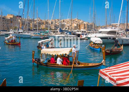 Taxi d'acqua la Valletta, vista dei tradizionali taxi d'acqua maltesi (dghajsa) da la Valletta arrivando al lungomare del porto turistico di Vittoriosa, Malta Foto Stock