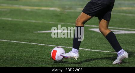 Un giocatore con equipaggiamento nero colpisce abilmente una palla da calcio su un tappeto erboso ben tenuto. Foto Stock
