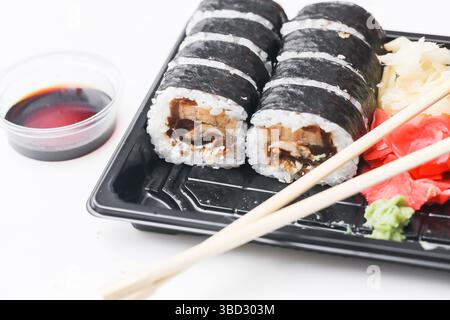 Panini di sushi con salsa di soia. Bacchette e zenzero sul vassoio nero Cibo giapponese da asporto. Maki fresco con alghe. Pranzo da asporto con cucina asiatica. Foto Stock