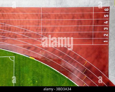 Veduta aerea di una pista da corsa rossa con corsie segnate e linee curve. Stadio sportivo con parte di un campo da calcio verde. Sport e. Foto Stock