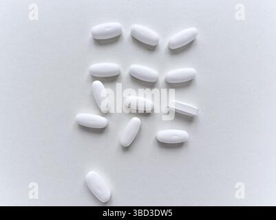 Una pillola bianca si trova su una superficie bianca. Ci sono molte pillole bianche sulla superficie. Le pillole sono tutte della stessa dimensione e forma Foto Stock